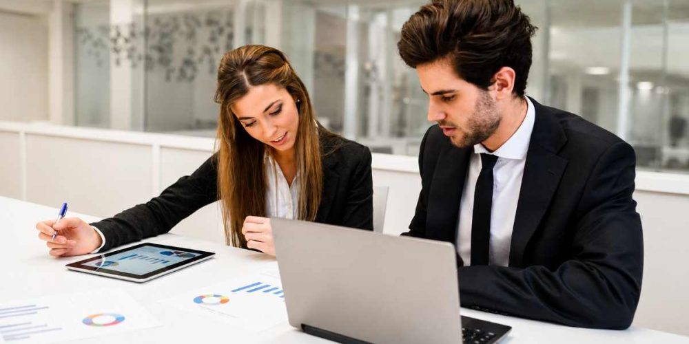 Two professionals reviewing reports and data on a laptop and tablet, representing the path to becoming a CQI IRCA Certified Auditor or Lead Auditor.